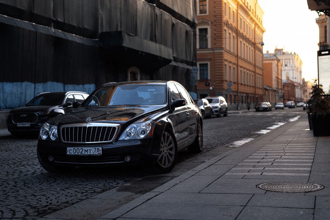 services-01 A luxurious black Maybach car parked on a cobblestone street in an urban setting at sunset.